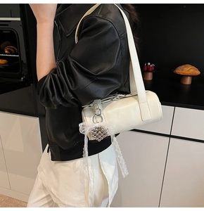 Detail of a creamy white cylindrical shoulder bag featuring heart beads and lace bow
