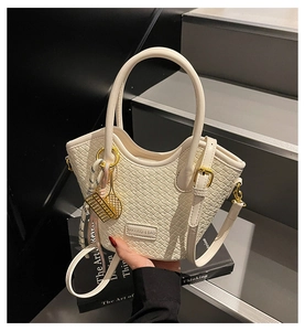 Détail du sac seau tissé blanc cassé avec pendentifs dorés et plaque de marque