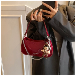 Detail view of burgundy patent leather baguette bag with silver chain and cartoon pendant