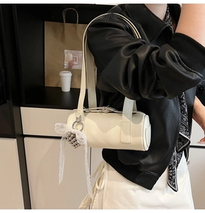 Close-up of white cylindrical shoulder bag with lace bow and silver bead pendant detail