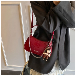 Detail of burgundy patent leather shoulder bag with silver chain and cute doll pendant