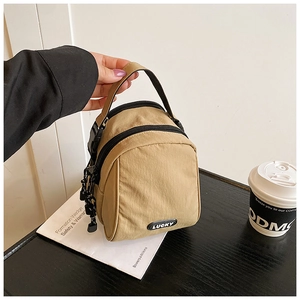 Detail shot of khaki mini nylon handbag with Lucky badge and dual zipper compartments