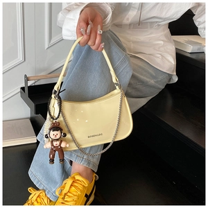 Detail of yellow patent leather underarm bag with metal chain and cartoon charm