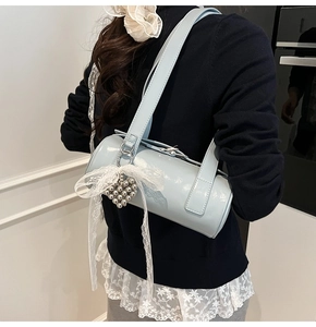Detail of light blue cylinder bag with glossy finish and silver heart-shaped bead charm