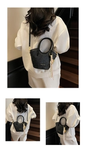 Détail du sac seau noir tressé avec plaque logo dorée et décoration de pompon chic