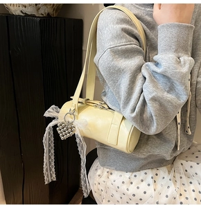 Detail of beige cylinder bag featuring silver heart beads and elegant white lace bow charm