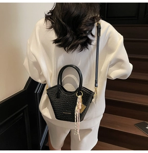 Détail d'un sac seau noir tressé avec plaque logo dorée et pompon décoratif élégant