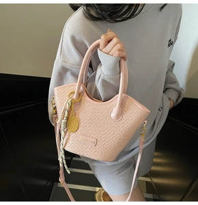 Détail d'un sac seau rose tressé avec breloque raquette de tennis et plaque logo en métal