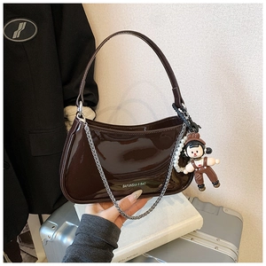 Detail of glossy brown patent leather hobo bag with silver chain and cute doll pendant