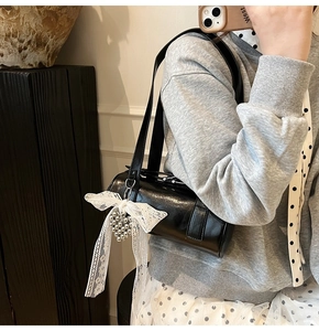 Detail view of black glossy baguette bag with white lace bow and beaded heart charm