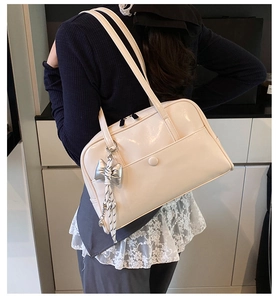 Detail of minimalist cream PU leather tote bag featuring a silver bow charm and large capacity