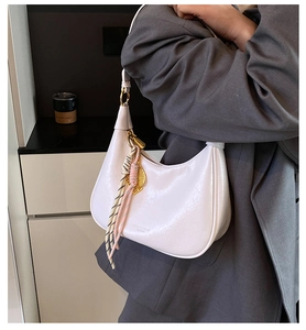 Detail of white oil wax leather hobo bag with gold hardware and woven tassel charm