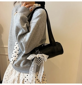 Detail of black cylindrical pillow bag featuring a large white lace bow and heart pendant