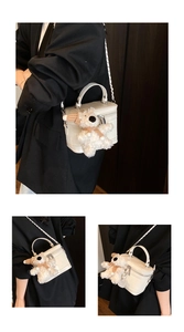 Close-up of a white box-shaped crossbody bag with a plush bear charm and chain strap