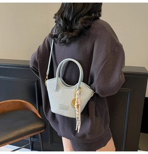 Détail d'un sac seau bleu clair tressé avec foulard en soie et étiquette en métal doré