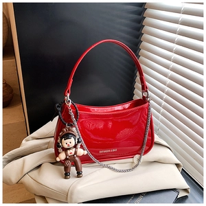 Detail of red patent leather handbag with silver chain and cute doll pendant on beige blazer