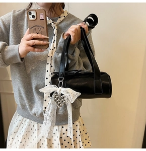 Detail of black cylindrical shoulder bag with white lace bow and silver heart charm