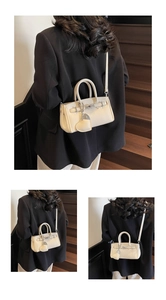 Detail of lychee textured cream handbag with metallic bar lock and heart charm