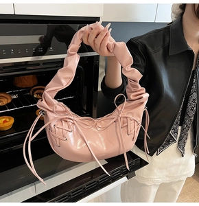 Détail d'un sac à main rose brillant avec bandoulière plissée et nœud sur le côté
