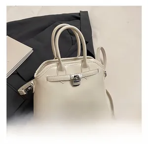 Detail of a creamy white shell handbag with metallic lock and leather strap accents