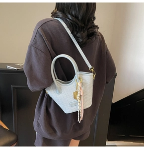 Sac seau bleu clair tressé avec pompon et détails dorés porté par un mannequin
