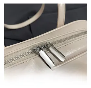 Close-up of dual silver metal zippers and smooth beige leather texture on the handbag