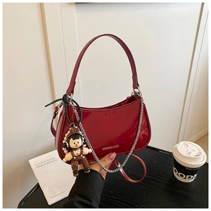 Detail of glossy red patent leather handbag with silver chain and cute doll charm