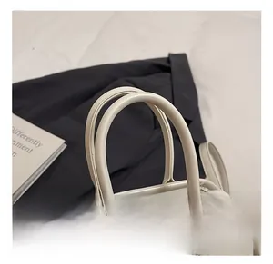 Detailed close-up of the smooth beige oil wax leather handles and fine stitching on the bag