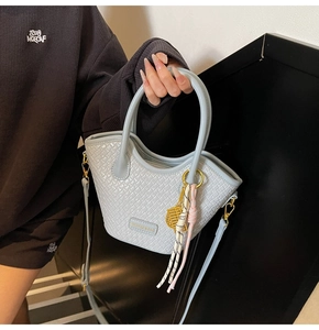 Détail de la texture tressée bleu clair et du logo en métal du sac seau demi-lune