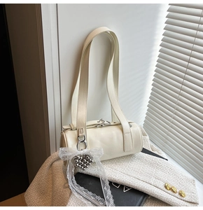 Detail of cream baguette bag with silver heart charm and lace bow on tweed jacket