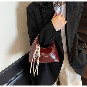 Detail of burgundy glossy leather handbag with gold logo and decorative tassel ornament