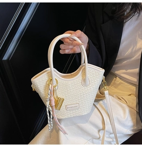 Détail du sac seau blanc tressé avec texture cuir et pendentif boulier doré élégant