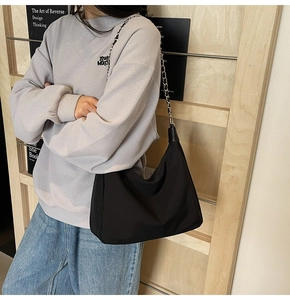 Detail einer schwarzen Halbmond-Schultertasche mit silberner Kette auf Freizeitoutfit