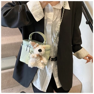 Detail of mint green cylindrical box bag with woven texture and a cute bear charm