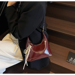 Detail of burgundy patent leather shoulder bag with tennis racket charm and gold logo