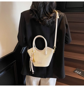 Détail du sac seau tressé avec pompon décoratif sur fond de costume noir élégant