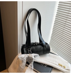 Detail of a black cylinder bag with heart charms and lace bows on a stylish outfit