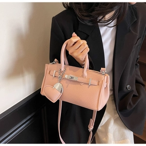 Detailed close-up of pink litchi grain leather handbag with gold metal twist lock and heart charm