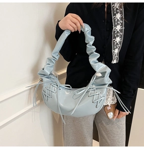 Détail du sac demi-lune bleu clair verni avec poignée froncée et nœuds latéraux