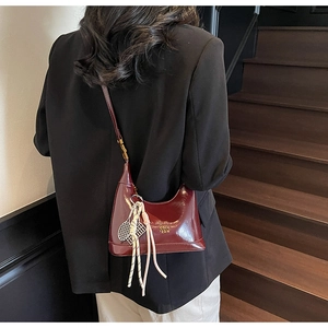 Detail view of burgundy oil wax leather dumpling bag with tennis racket charm and gold logo
