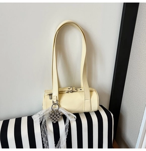 Detail of cream yellow cylinder shoulder bag with heart pendant and white lace ribbon