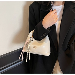 Close-up of cream white glossy leather bag with gold logo and decorative woven charm