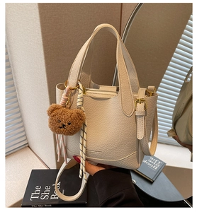 Detail of beige lychee pattern bucket bag with teddy bear charm and adjustable strap