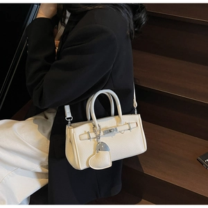 Detail of cream lychee pattern handbag with silver clasp and heart charm on a model