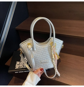 Détail du sac seau argenté tressé avec logo métallique et pendentif foulard en soie