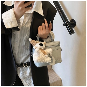 Detail view of light blue box bag featuring woven texture and cute plush bear charm