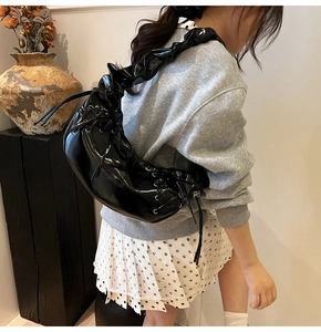 Détail du sac à épaule en cuir verni noir avec cordon de serrage et bandoulière plissée