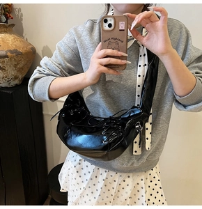 Selfie miroir montrant un sac demi-lune en cuir verni noir avec détails de laçage