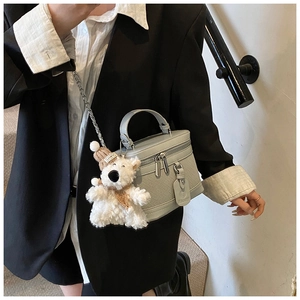 Detail of grey box bag with woven texture, silver zipper and cute teddy bear charm