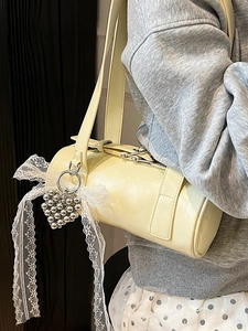 Cream cylinder baguette shoulder bag with heart charm and lace detail on a model